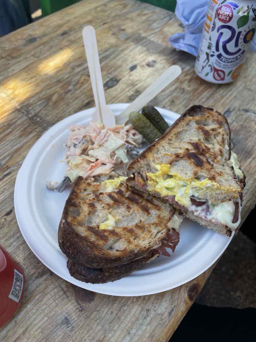 A cut melt on a paper plate with slaw and gherkins on a market bench