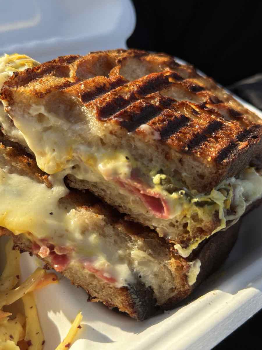 Close-up of a griddle-pressed melt with char lines and cured meat, cheese oozing at the seam